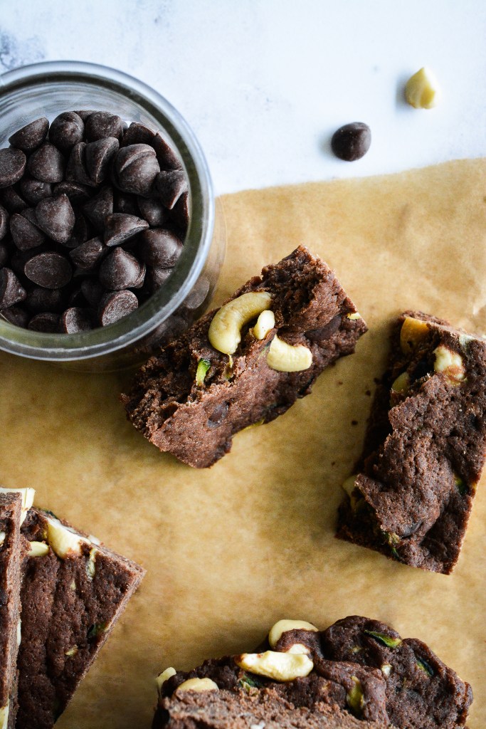 A close-up view of chocolate nutty rice crispy treats with cashews, surrounded by chocolate chips and placed on a parchment paper background.